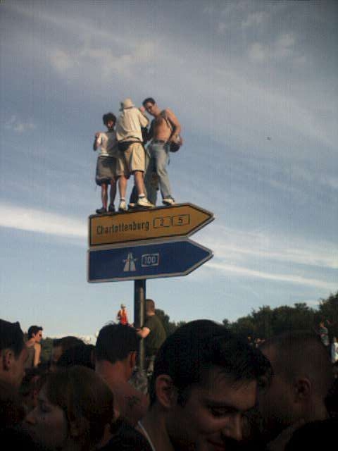 Vier Menschen auf dem Wegweiser Richtung Charlottenburg und auf dem Wegweiser zur Autobahn A 100, Photo vom Abend der Loveparade in Berlin am 21.07.2001